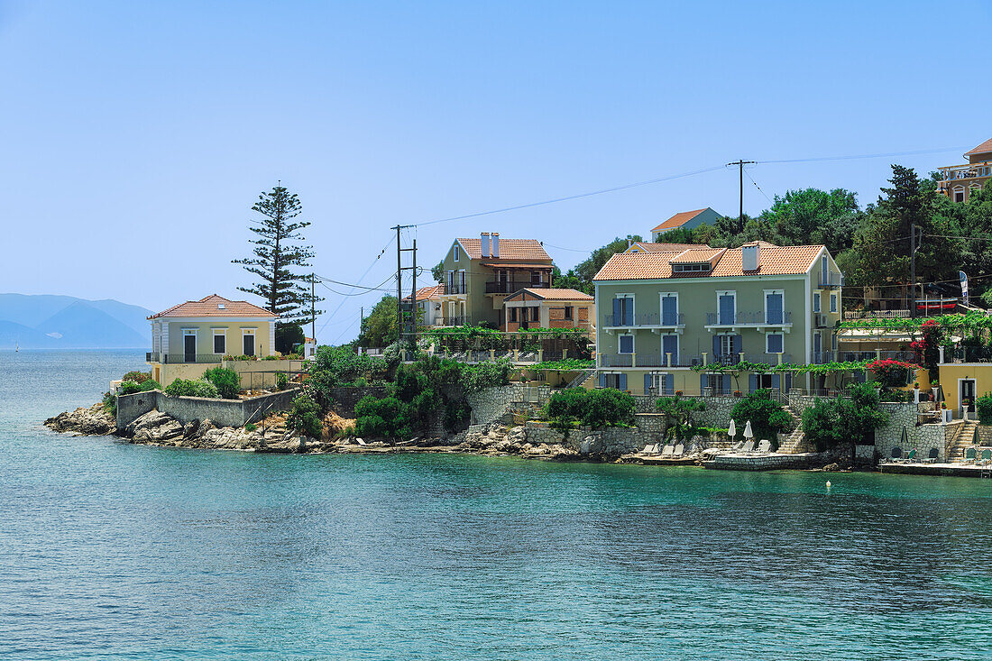 Fiscardo Dorf mit niedrigen Häusern mit roten Ziegeldächern an einem Strand mit Badenden, Fiscardo, Kefalonia, Ionische Insel, Griechische Inseln, Griechenland, Europa