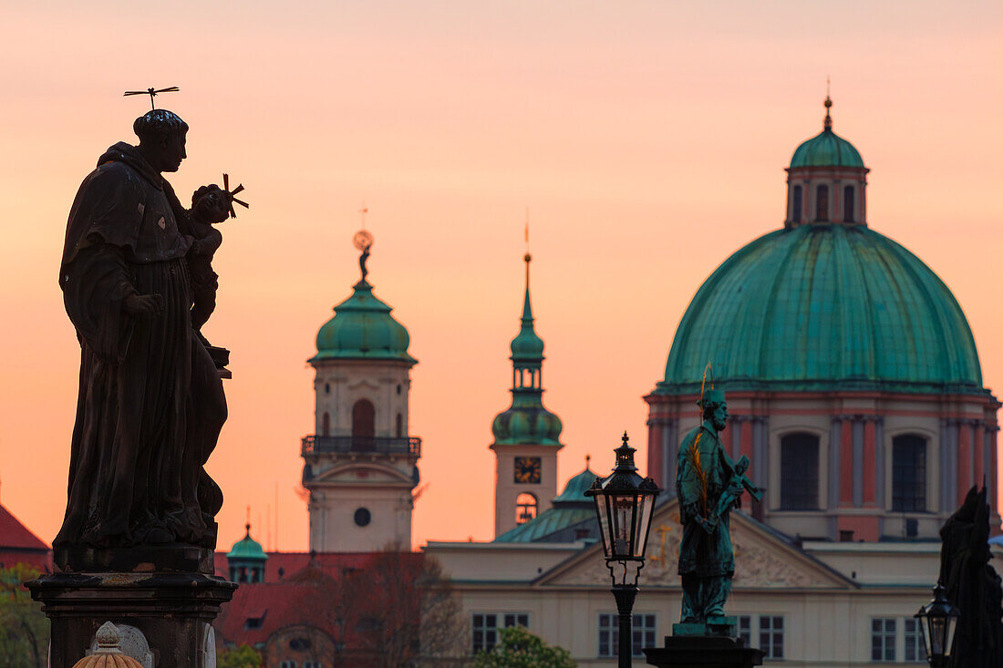 Statue an der Karlsbrücke mit der Kuppel des Heiligen Franz von Assisi im Hintergrund bei Sonnenaufgang, UNESCO-Welterbe, Prag, Tschechische Republik (Tschechien), Europa