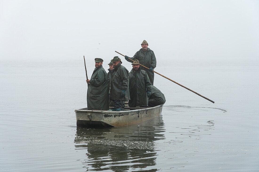 Gruppe von Fischern auf einem Boot, die sich am nebligen Morgen auf die Fischernte vorbereiten, Rozmberk-Teich, UNESCO-Biosphäre, Trebon, Bezirk Jindrichuv Hradec, Südböhmische Region, Tschechische Republik (Tschechien), Europa