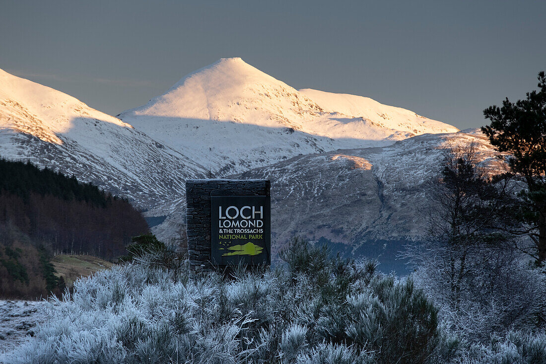 Schild des Loch Lomond and Trossachs National Park mit Ben More und den Crianlarich Hills dahinter im Winter, Loch Lomond and Trossachs National Park, Schottische Highlands, Schottland, Vereinigtes Königreich, Europa