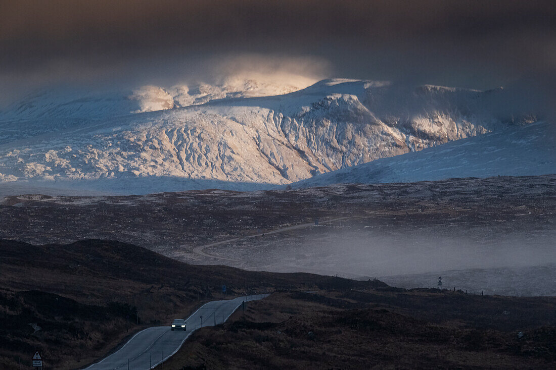 Ein Auto überquert Rannoch Moor auf der A82 Trunk Road in der Abenddämmerung mit Beinn a Chreachain und den Grampian Mountains im Hintergrund, Rannoch Moor, Argyll und Bute, Schottische Highlands, Schottland, Vereinigtes Königreich, Europa