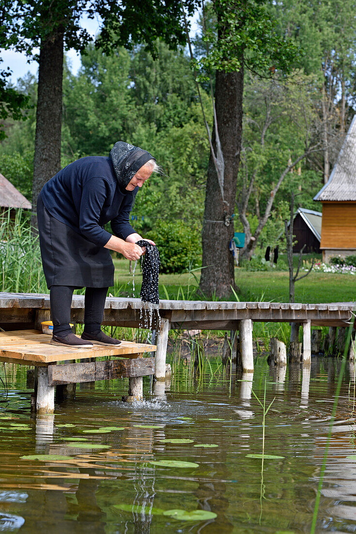 Alte Frau beim Wäschewaschen vor ihrem Haus am Baluosykstis-See bei Ginuciai, Aukstaitija-Nationalpark, Litauen, Europa