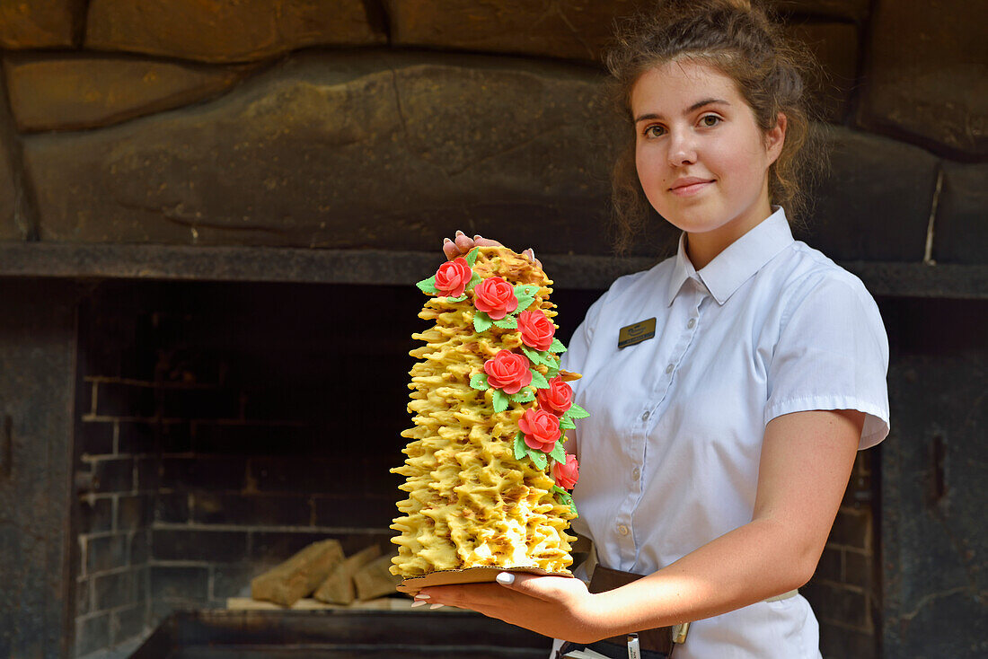 Young waitress presenting a famous cake named Sakotis in a decorated version at Romnesa bakery-restaurant at Strigailiskis, Ignalina district, Aukstaitija National Park, Lithuania, Europe