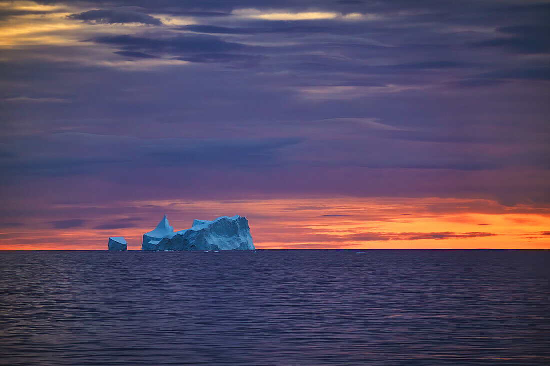 Eisberg vor orangefarbenem Abendhimmel, Antarktis, Polarregionen