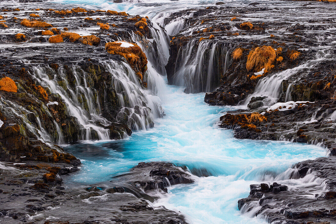 Die unglaublich farbenfrohen Details des berühmten Bruarfoss-Wasserfalls, mit seinem türkisfarbenen Wasser und dem goldenen Gras, aufgenommen an einem kalten Wintertag, Island, Polarregionen