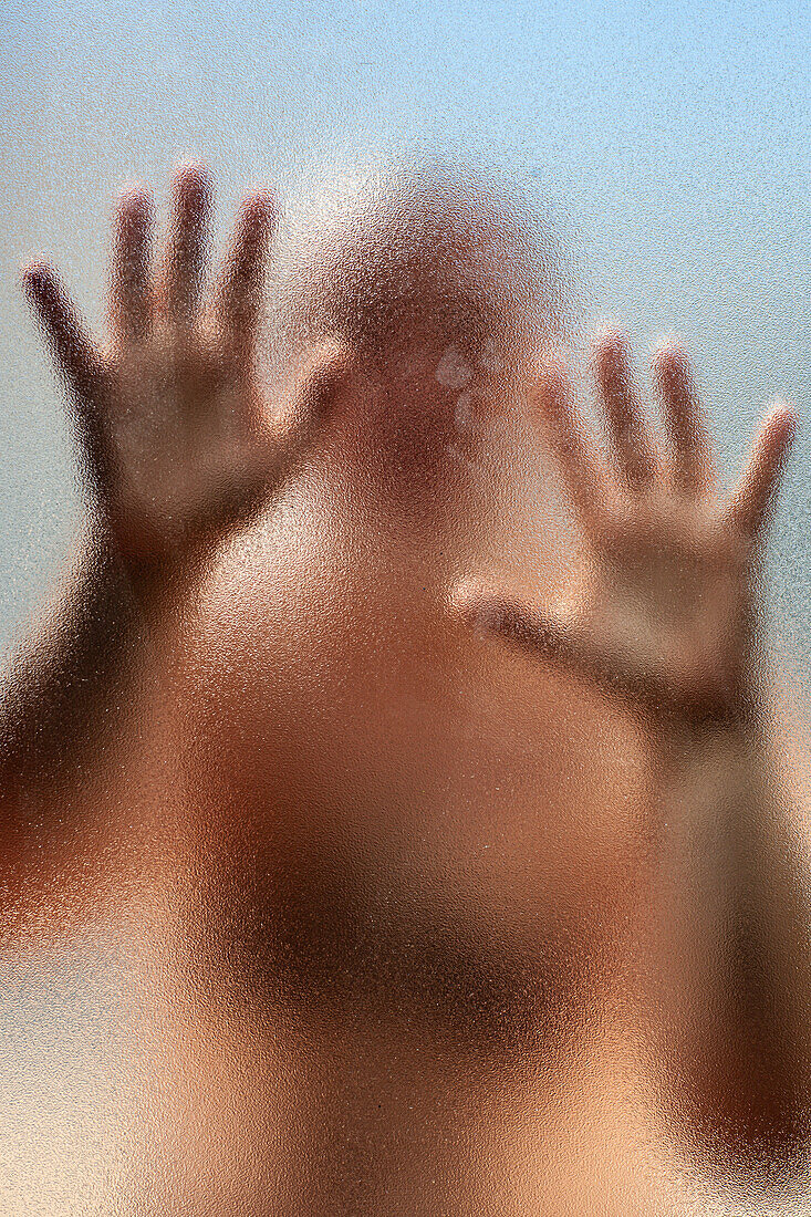 A man is trapped behind a frosted glass panel with his hands pressed against the surface, creating a sense of confinement and isolation.