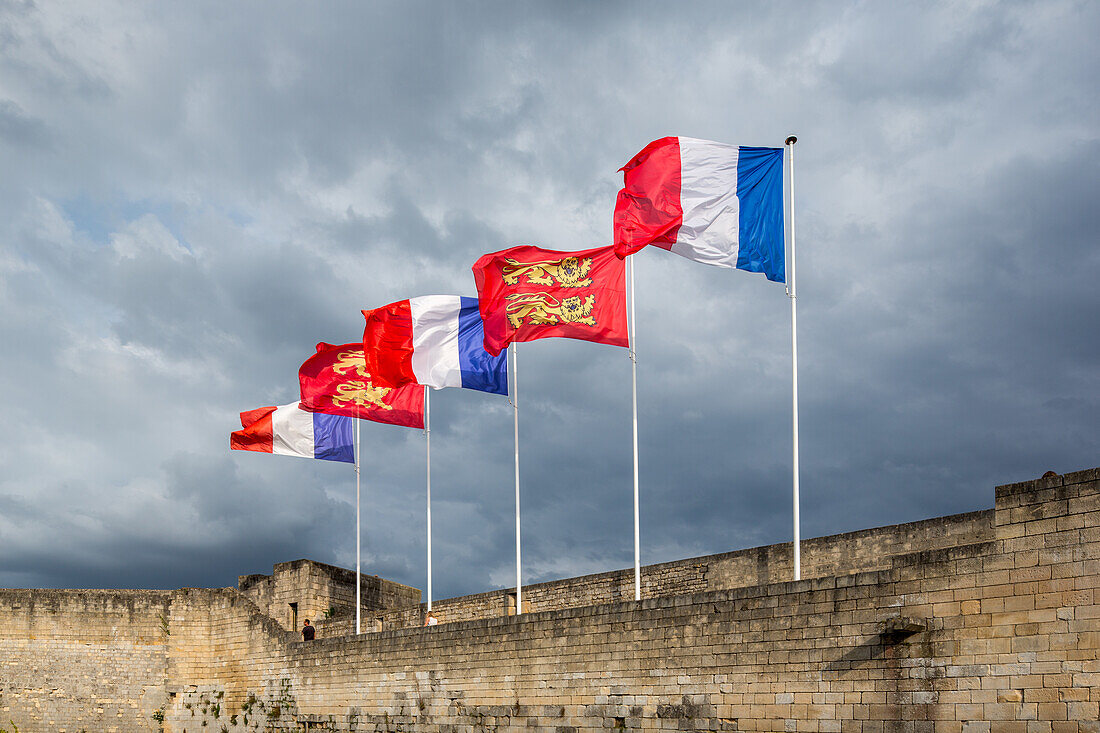 Die Flaggen der Normandie und Frankreichs wehen auf der historischen Burg von Caen in der Normandie, mit bewölktem Himmel im Hintergrund.