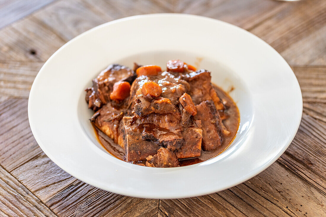 Nahaufnahme des traditionellen andalusischen Eintopfs Rabo de Toro, der in einer weißen Schale serviert wird und sein reichhaltiges und herzhaftes Aussehen unterstreicht.