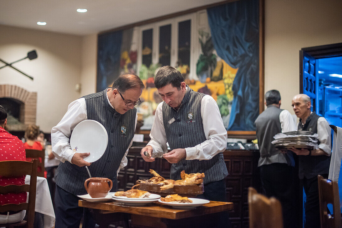 Waiters serving roast suckling pig at the renowned Jose Maria restaurant in Segovia, Castilla y Leon, Spain. A vibrant and traditional dining experience.