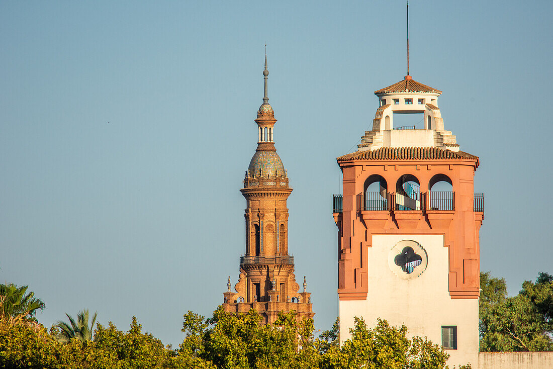 Historic towers of Torre del Pabellón de Chile and Plaza de España amidst lush trees in María Luisa Park, Seville, Andalucía, Spain.