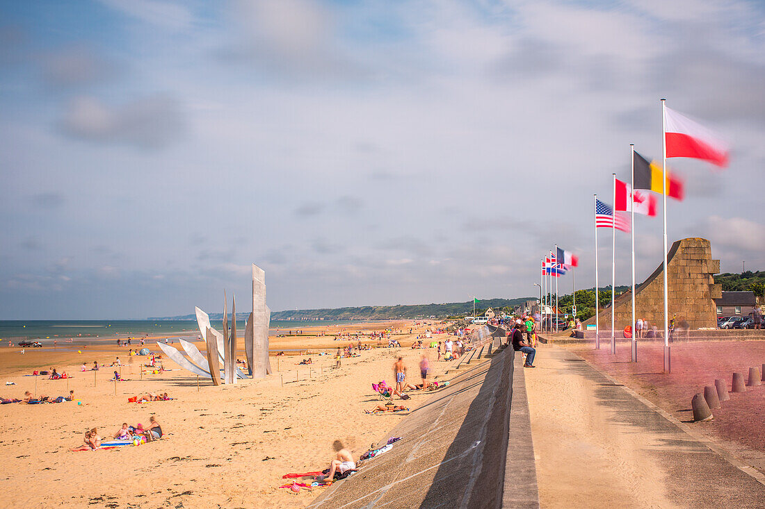 Langzeitbelichtung von Omaha Beach in der Normandie, Frankreich, mit vielen Nationalflaggen und Strandbesuchern an einem sonnigen Tag.