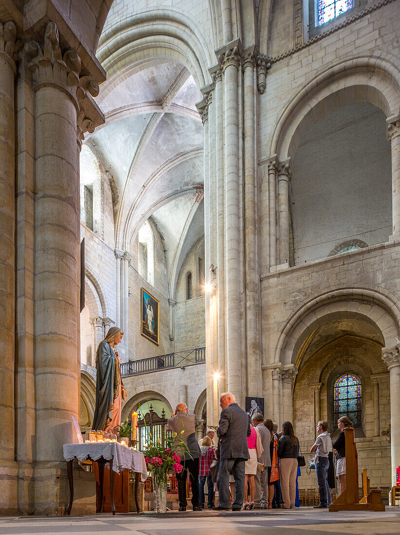 A group of people inside the historic Men's Abbey Church of Saint Etienne in Caen, Normandy. The church interior features stunning architecture and religious statues.