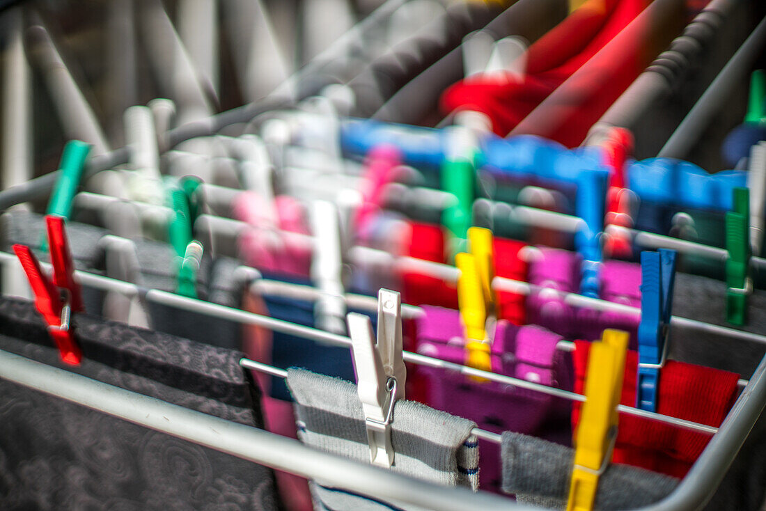 Close-up of colorful clothespins securing various clothing items on a drying rack. Vibrant clothes drying indoors with a soft background blur.