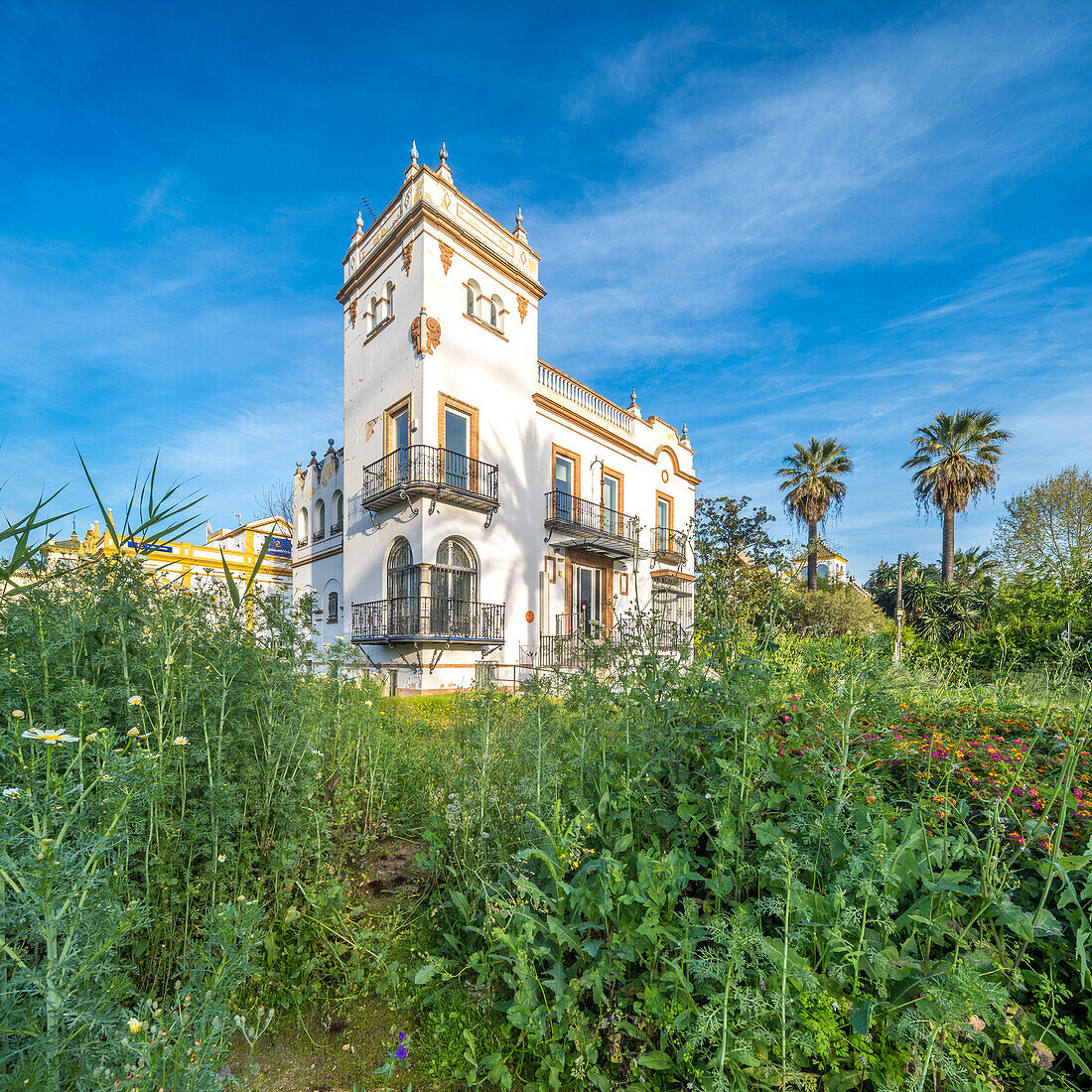 Abandoned regionalist style chalet located on Avenida de la Palmera in Sevilla, Spain with lush overgrown vegetation.