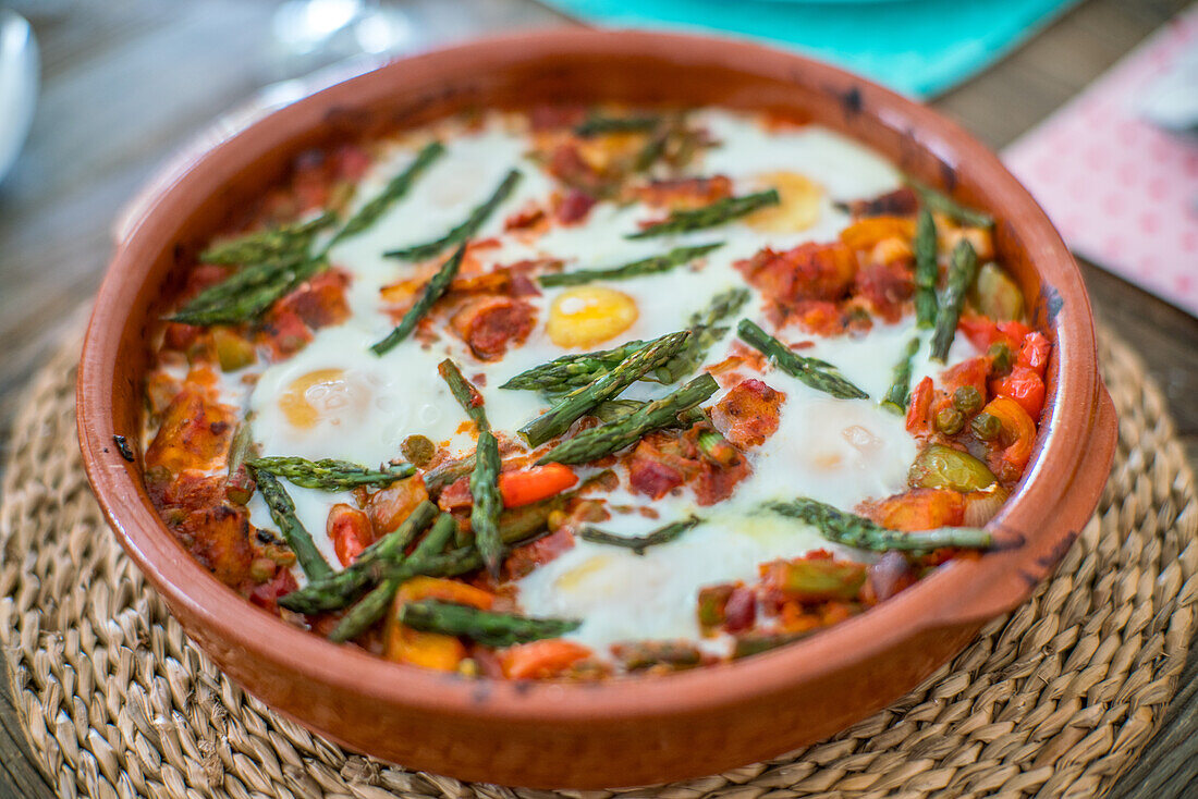 A traditional Andalusian dish, huevos a la flamenca, served in a clay pot with asparagus, peppers, and tomatoes.