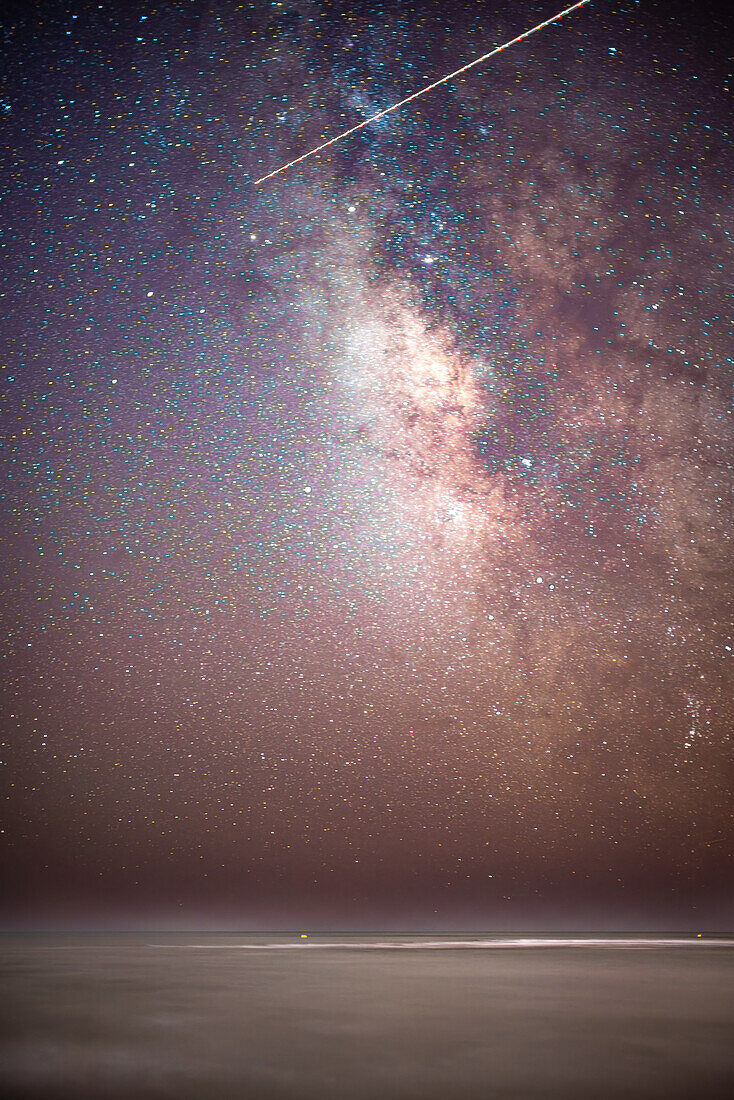 Starry night sky featuring the Milky Way over the calm Atlantic Ocean at Isla Canela Beach, Ayamonte, Spain.