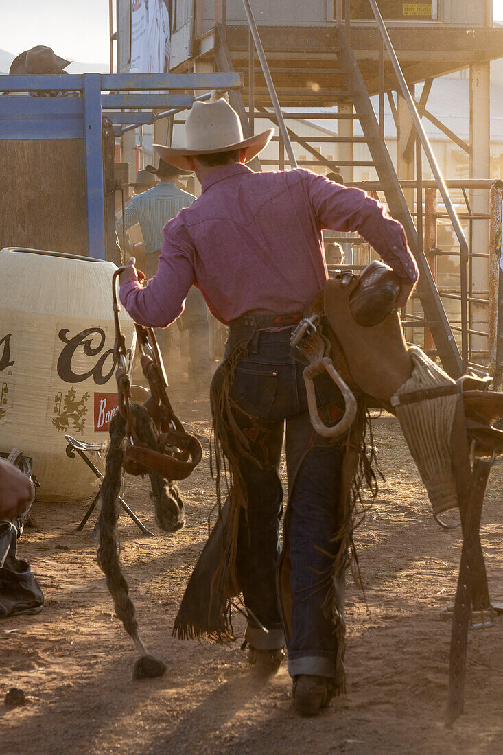 A saddle bronc cowboy carries his special bucking saddle to the bucking chutes at a rodeo in rural Utah.