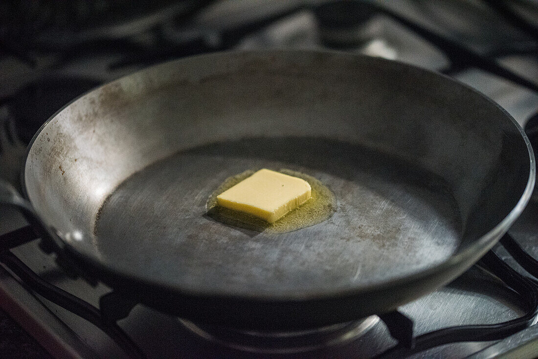 A close-up view of a piece of butter melting in a traditional iron skillet in Seville, Spain.