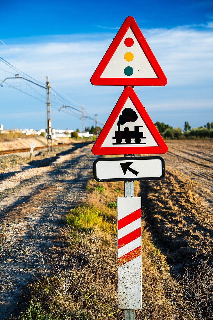 Warnschilder an einem Bahnübergang bei Carrion de los Cespedes in der Provinz Sevilla, Andalusien, Spanien. Ländliche Gegend mit Bahngleisen und klarem, blauem Himmel.