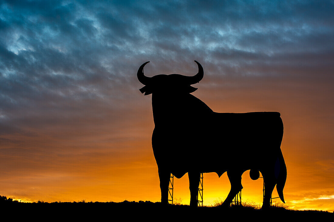 Atemberaubende Silhouette des berühmten Toro de Osborne vor einem leuchtenden Sonnenuntergang in Sevilla, Spanien.