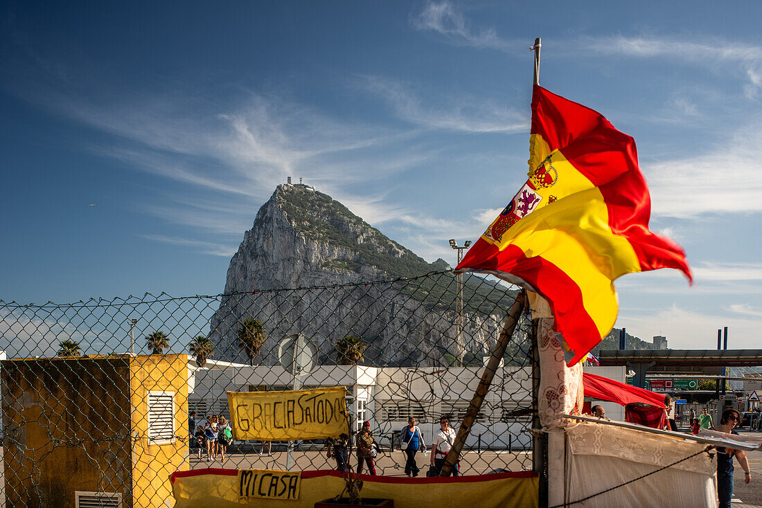 A protester with a Spanish flag stands near the border of Gibraltar, UK, with the famous rock formation in the background.