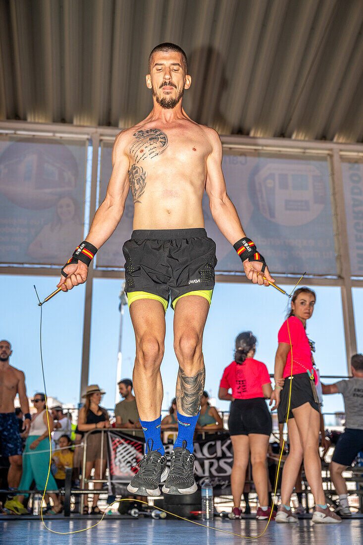 Konzentrierter Athlet beim Seilspringen während eines CrossFit-Wettbewerbs in Sevilla, Spanien. Demonstration von Fitness, Kraft und Ausdauer mit einer unterstützenden Menge im Hintergrund.