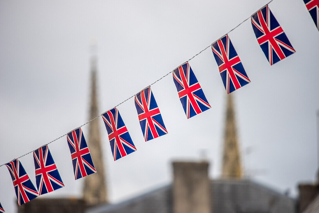 An einer Schnur aufgehängte Union-Jack-Flaggen mit einer verschwommenen Ansicht von Quimper, Bretagne, Frankreich, im Hintergrund.