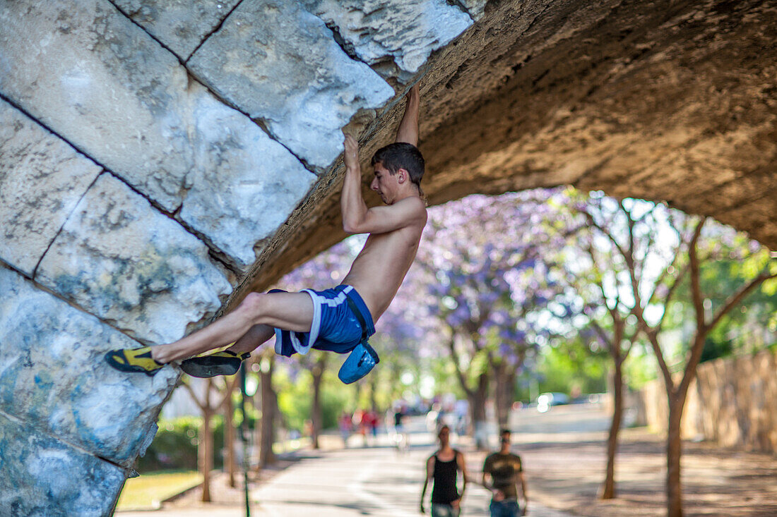 Young climber practicing free climbing under the iconic Triana Bridge in Sevilla, Andalusia, Spain. Displaying strength and determination.