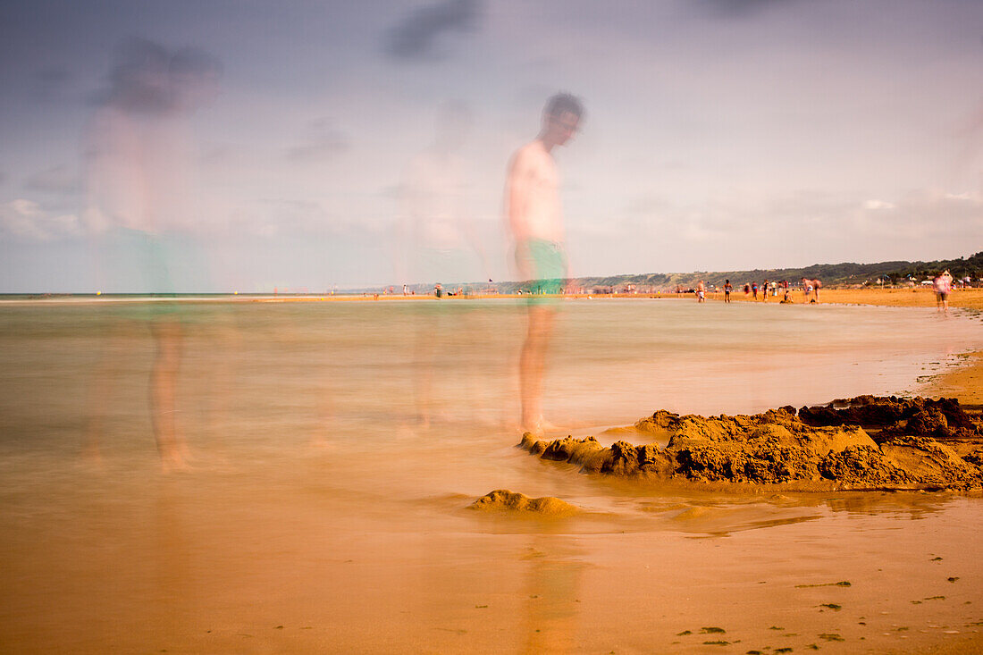 Long exposure photograph capturing the serene and historic Omaha Beach in Normandy, France with blurred figures on a calm day.