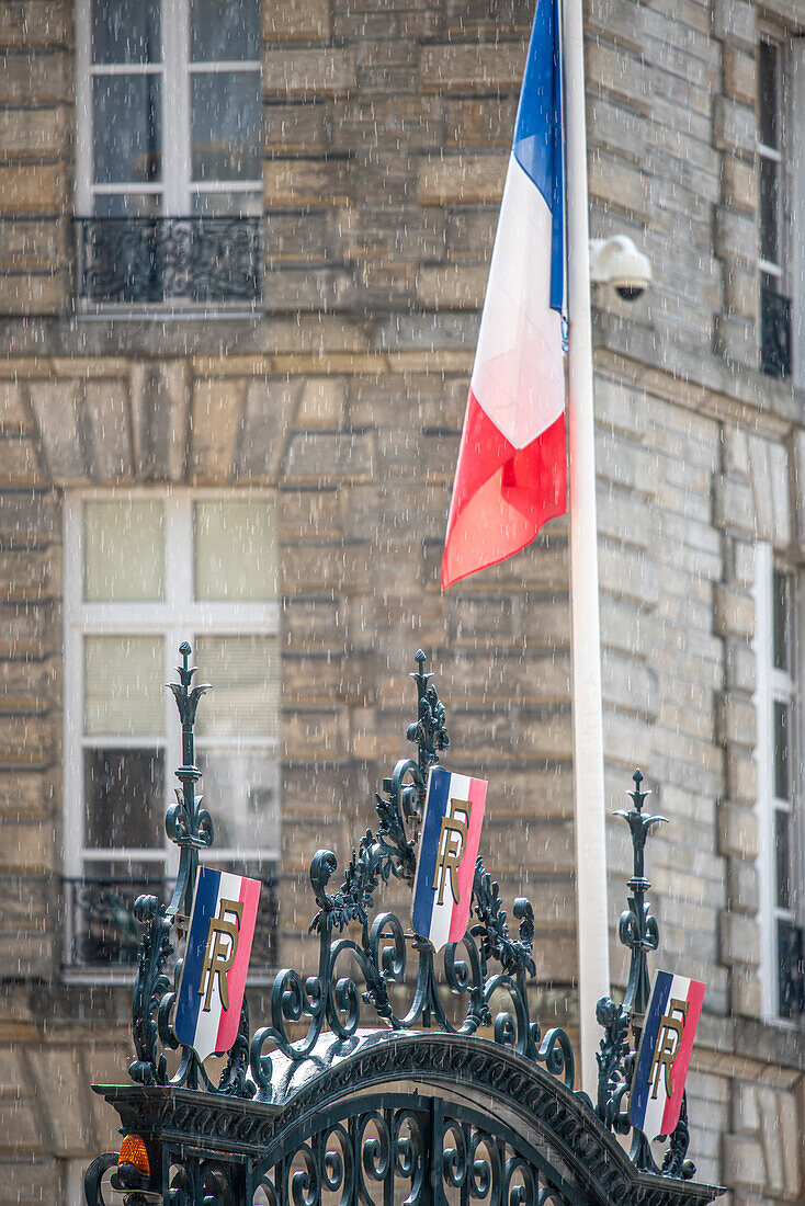 Die französische Flagge weht an einem regnerischen Tag vor dem verschnörkelten Tor eines historischen Gebäudes in Vannes, Bretagne, Frankreich.