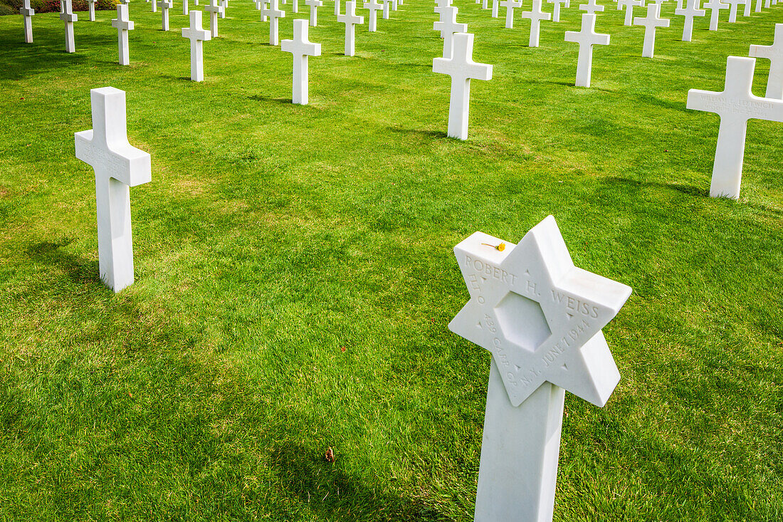 Reihen von weißen Kreuzen und ein Davidstern kennzeichnen Gräber auf dem amerikanischen Soldatenfriedhof in der Normandie, Frankreich. Ein Ort des feierlichen Gedenkens.