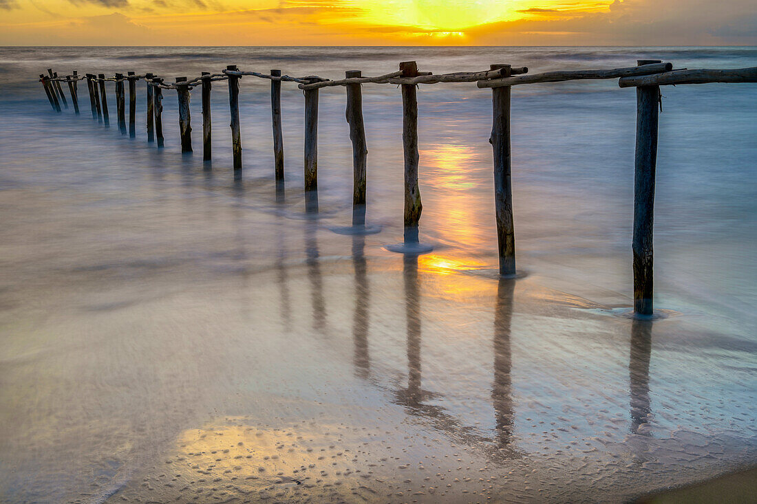 Atemberaubender Sonnenuntergang über einem ruhigen Strand mit einem Holzzaun, der die Grenze des Nationalparks Donana in Matalascanas, Almonte, Huelva, Andalusien, Spanien, markiert.