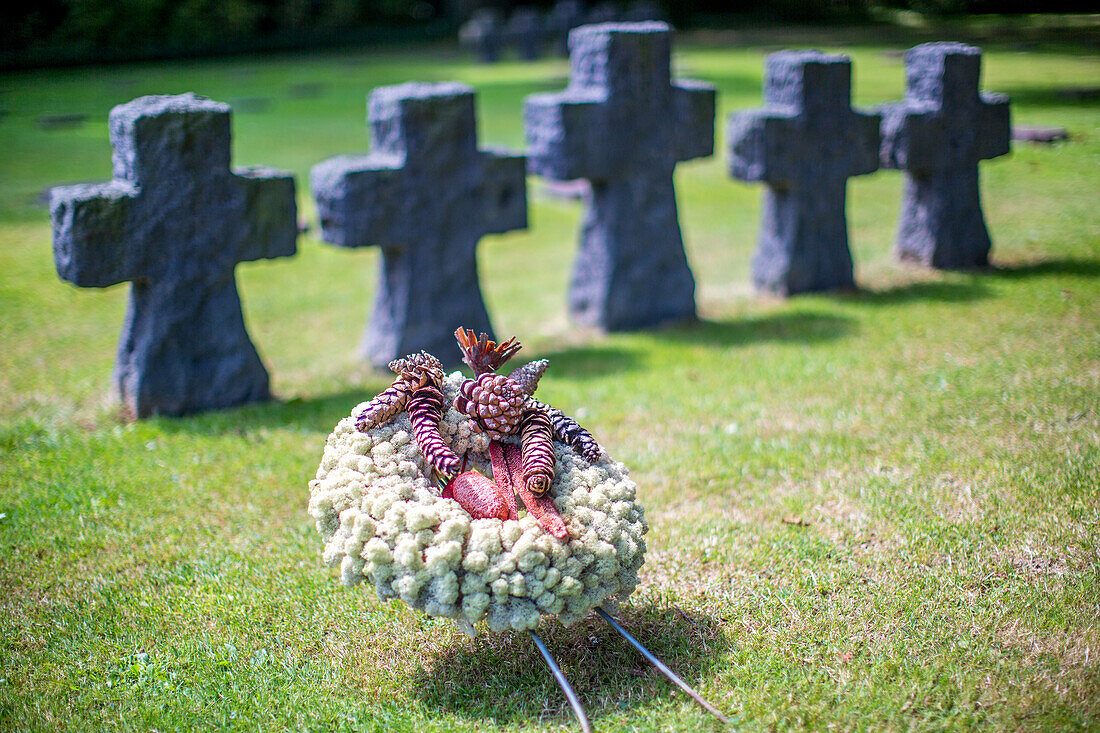 Eine düstere Szene auf dem deutschen Soldatenfriedhof in der Normandie, Frankreich, mit einem Gedenkkranz und Steinkreuzen.