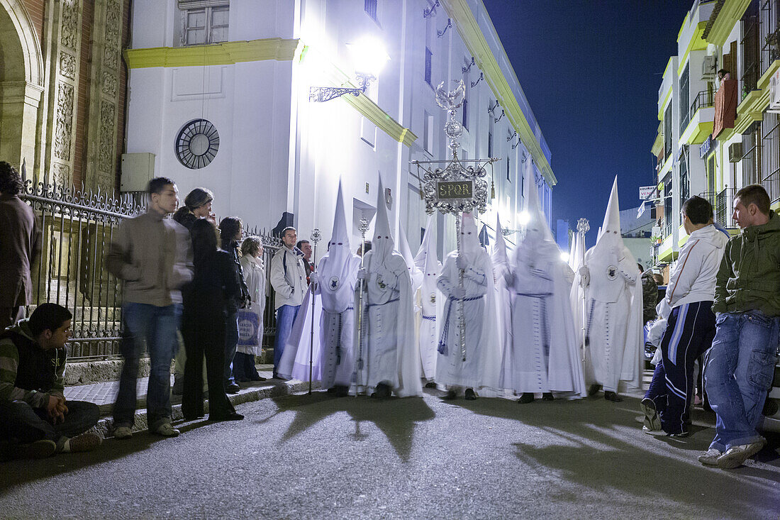 Nazarenos from the Resurrected Brotherhood during Easter Sunday morning procession in Seville, Spain. Nighttime religious tradition with spectators watching.