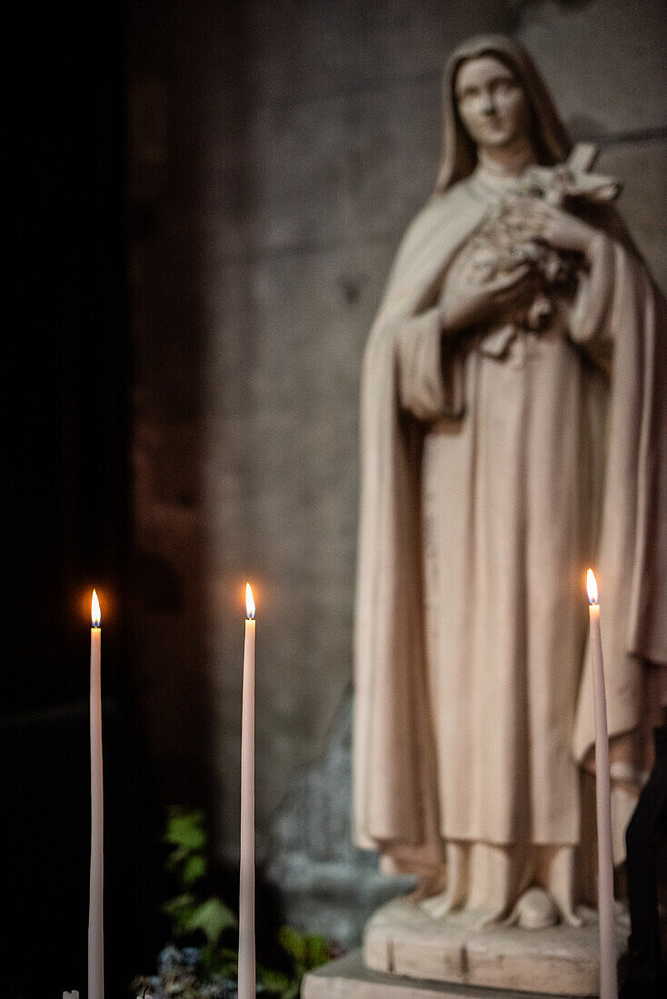 Drei brennende Kerzen vor einer Statue im Coll giale Saint-Aubin, Guerande, Frankreich, schaffen eine heitere und spirituelle Atmosphäre.