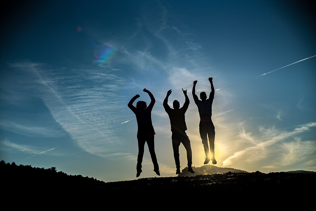 Eine Gruppe von Freunden feiert und springt bei Sonnenuntergang in Villaviciosa de Cordoba, Andalusien, Spanien. Silhouette vor einem schönen Himmel.