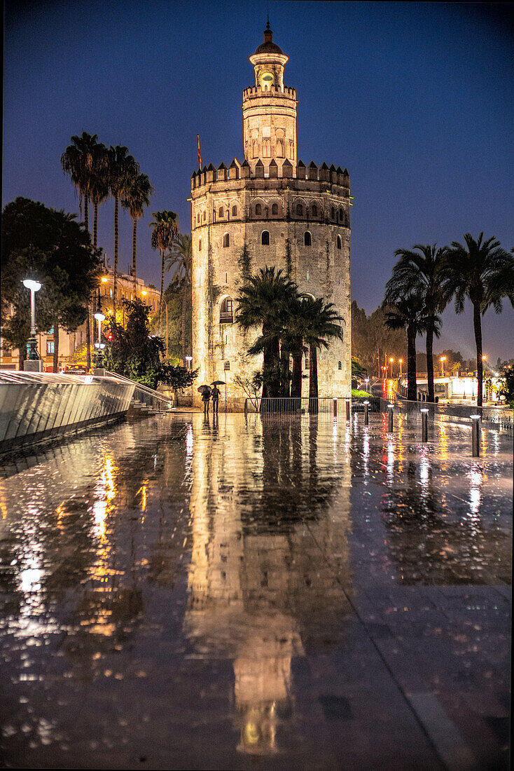 Der Torre del Oro in Sevilla, Andalusien, Spanien, spiegelt sich auf dem nassen Pflaster in einer schönen Regennacht.