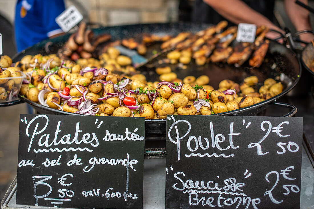 Auslage mit frischen gebratenen Kartoffeln und Hähnchen auf einem Straßenmarkt in Vannes, Bretagne, Frankreich. Verlockende Szene mit Straßenessen.