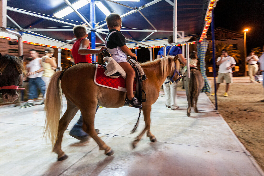 Children enjoying a pony ride on a night carousel in Sanlucar de Barrameda, Andalusia. Fun and excitement at a local fair.