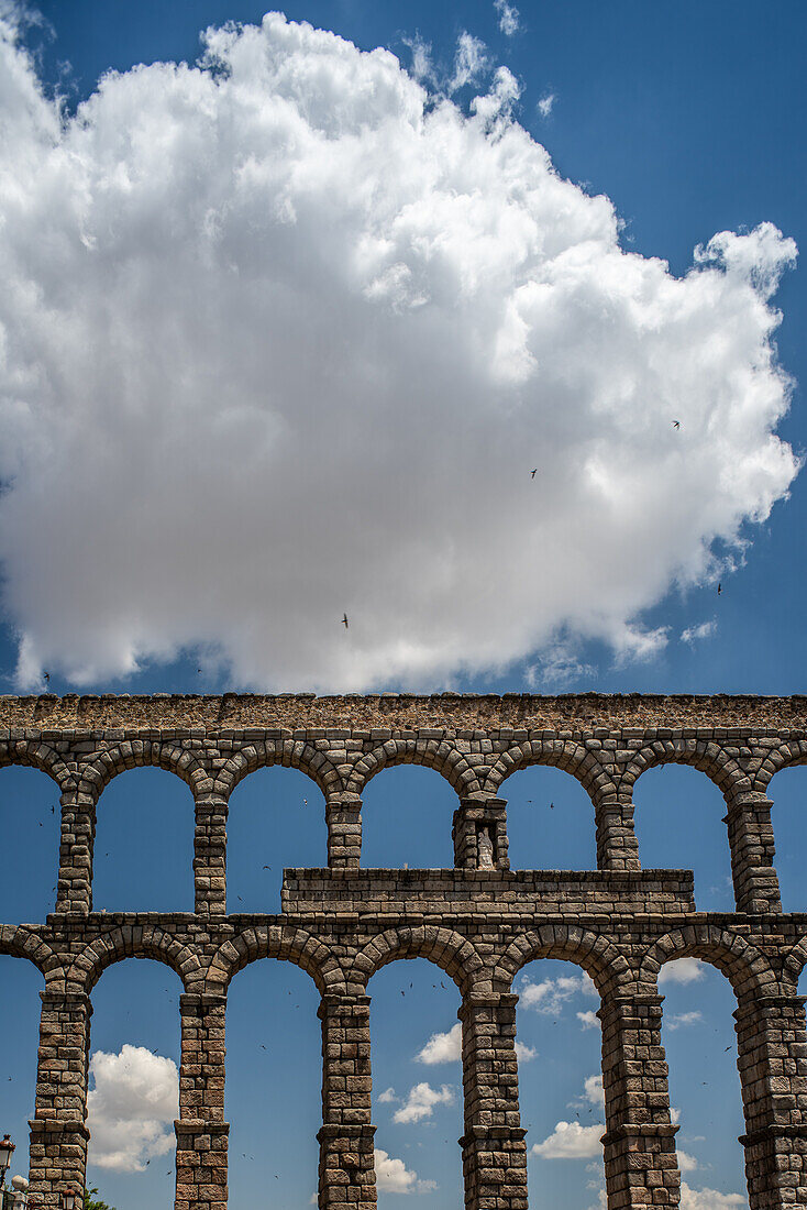 Historic Roman aqueduct in Segovia, Castilla y Leon, Spain. Featuring stone arches and a blue sky with clouds.