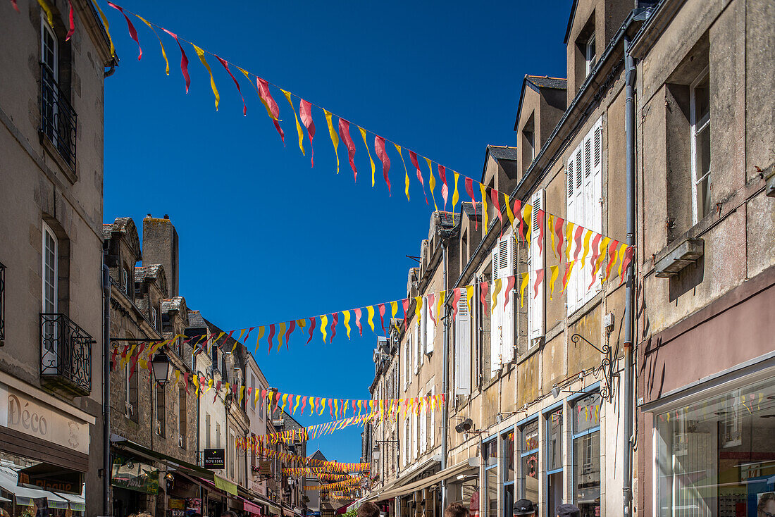 An einem sonnigen Tag hängen leuchtend rote und gelbe Fahnen in einer charmanten Straße in Guerande, Frankreich.