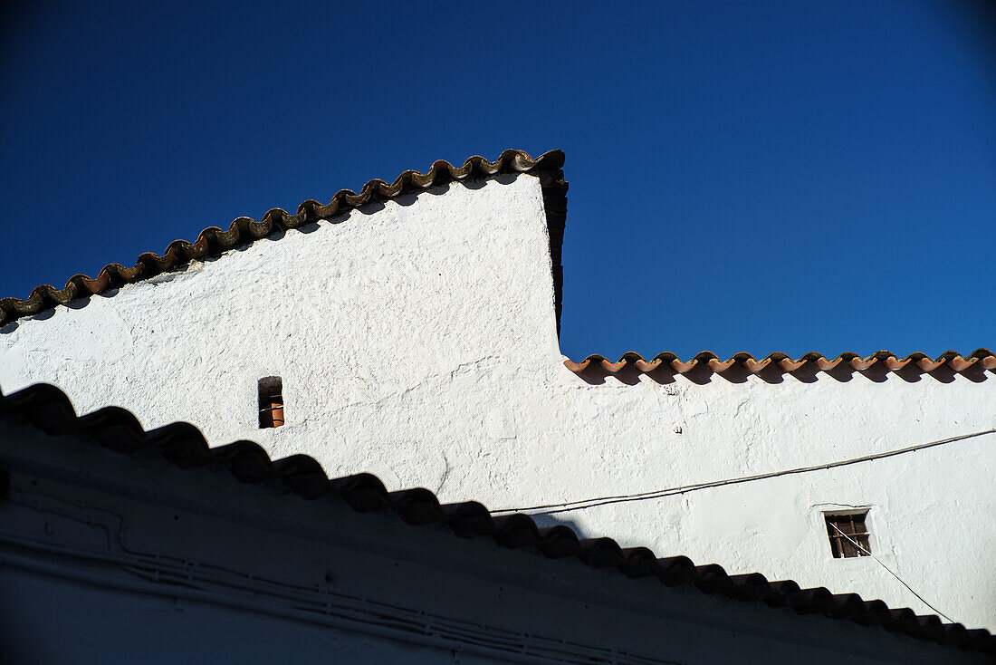 Blick auf ein traditionelles, weiß gekalktes Hausdach in Fuenteheridos in der Provinz Huelva, Andalusien, Spanien, bei strahlend blauem Himmel.