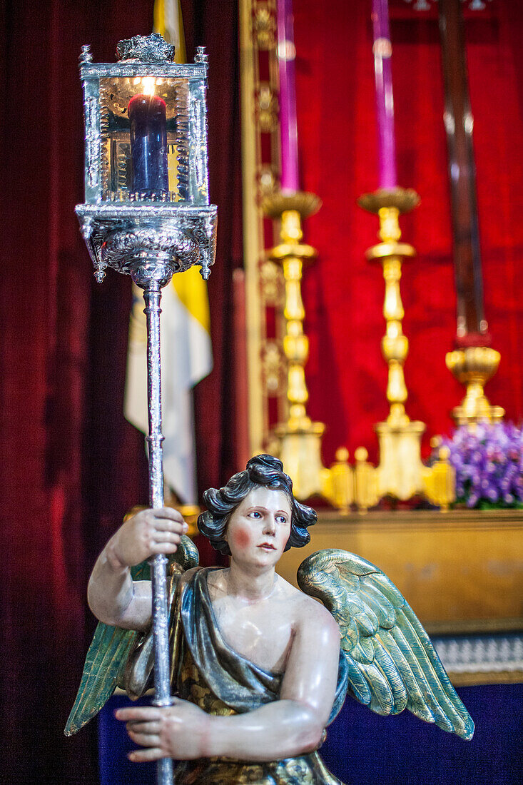 Nahaufnahme einer Engelsstatue in der Hermandad del Silencio in Sevilla, Spanien. Lebendige religiöse Dekorationen im Hintergrund.