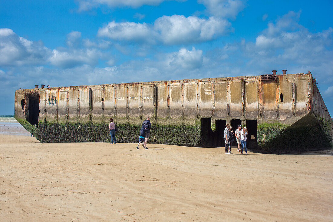 Touristen besuchen die Überreste des Artefakts Mulberry B am Gold Beach in Arromanches, Normandie, Frankreich, das die Geschichte und das Vermächtnis des Zweiten Weltkriegs zeigt.