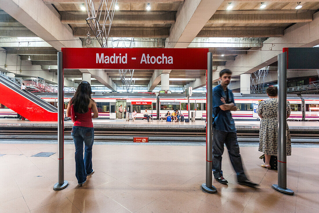 Madrid Atocha Station in Madrid, Spain, showcasing passengers waiting for a commuter train amidst modern architecture.