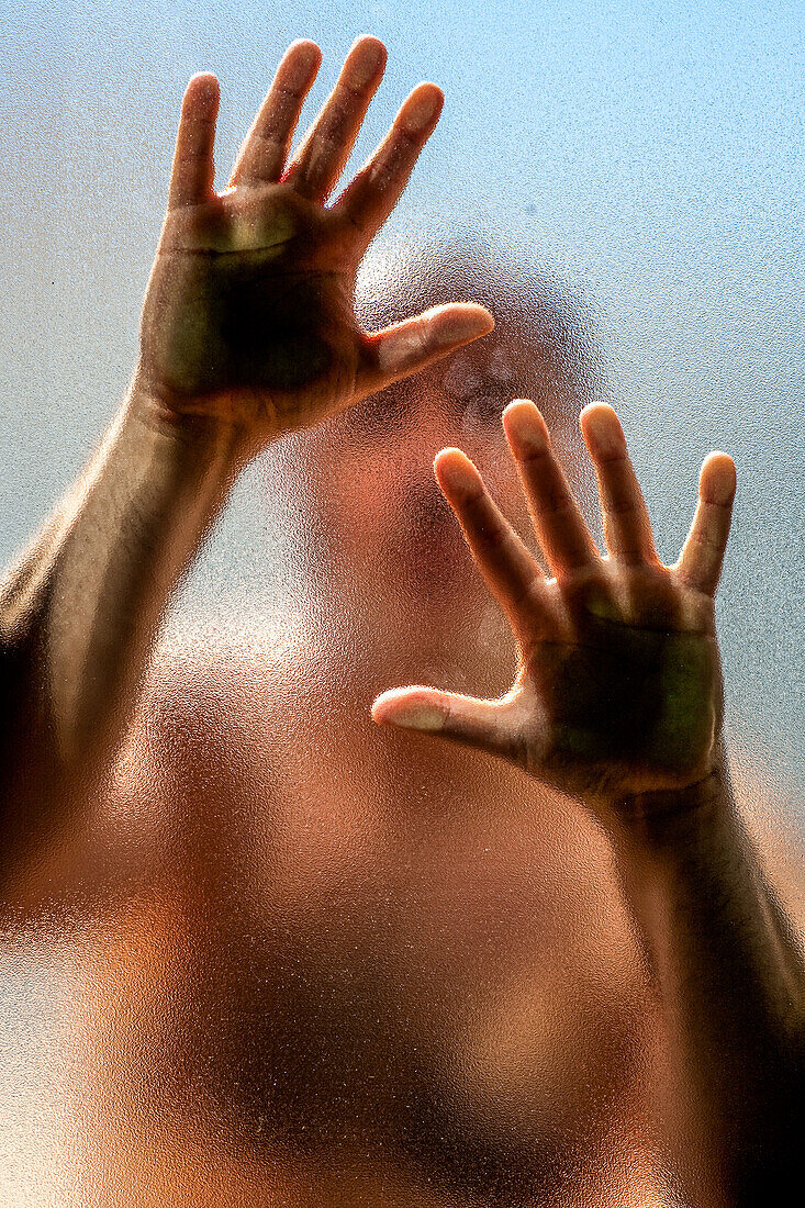 A man is trapped behind a frosted glass panel with his hands pressed against the surface, creating a sense of confinement and isolation.