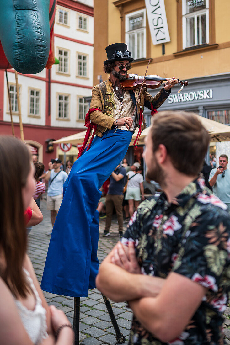 Künstlerin spielt Geige, während sie auf Stelzen bei der Puppenparade vom Marienplatz zum Altstädter Ring während des Prager Straßentheaterfestivals Behind the Door läuft, Prag, Tschechische Republik