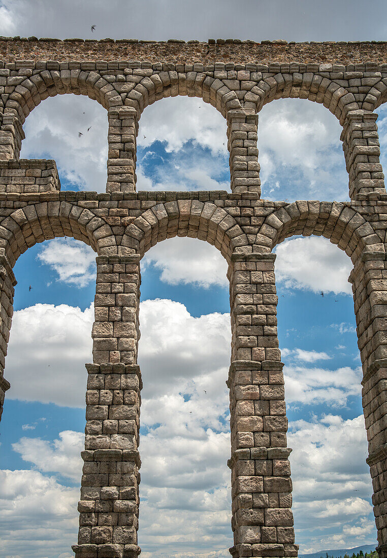 Atemberaubender Blick auf das antike römische Aquädukt in Segovia, Spanien, mit Bögen, die von einem klaren blauen Himmel und vereinzelten Wolken eingerahmt werden.