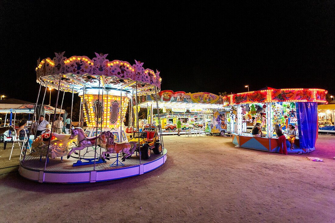 Beleuchtete Kinderkarussells am nächtlichen Strand von Sanlucar de Barrameda, Andalusien, Spanien. Eine lebhafte und lustige Atmosphäre für Familien und Freunde.