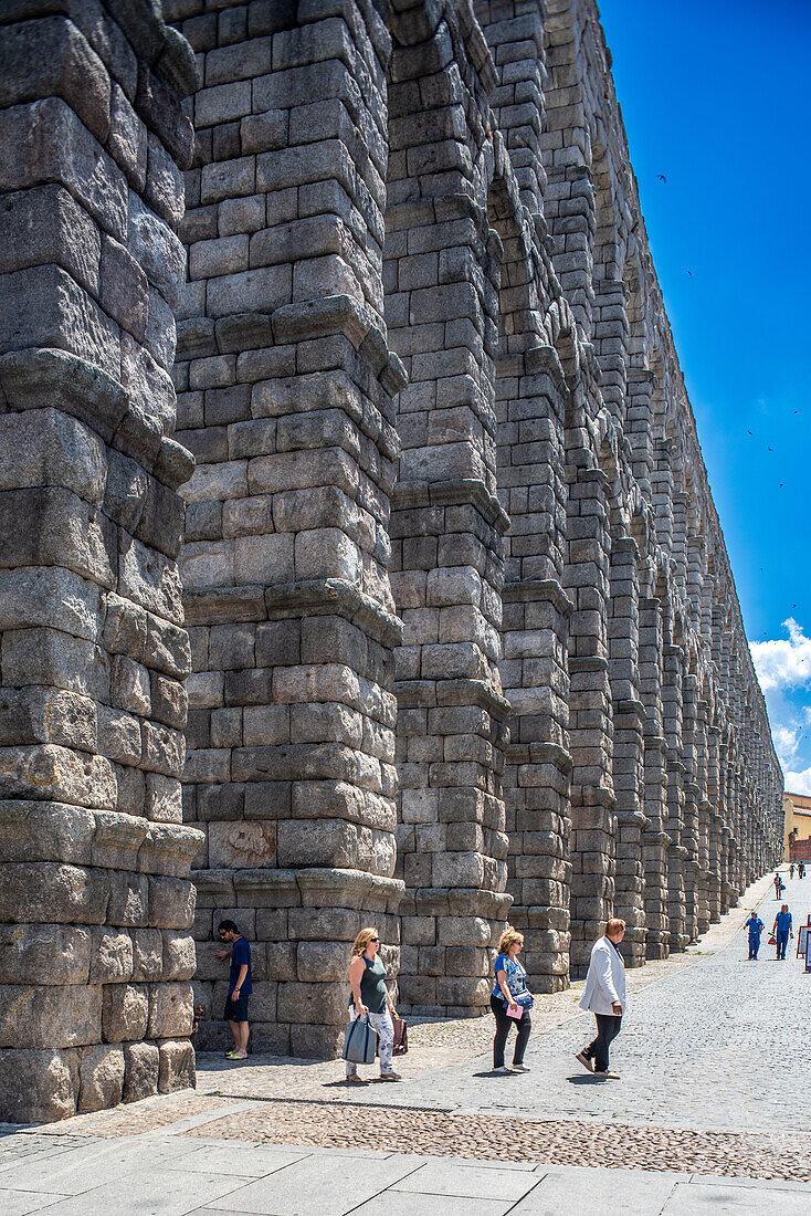 Besucher erkunden das historische römische Aquädukt in Segovia, Castilla y Leon, Spanien, an einem strahlenden Sonnentag.